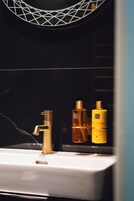A bathroom with a white sink, a gold faucet, and two bottles of lotion.