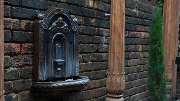 A water fountain with intricate metalwork against a brick wall.