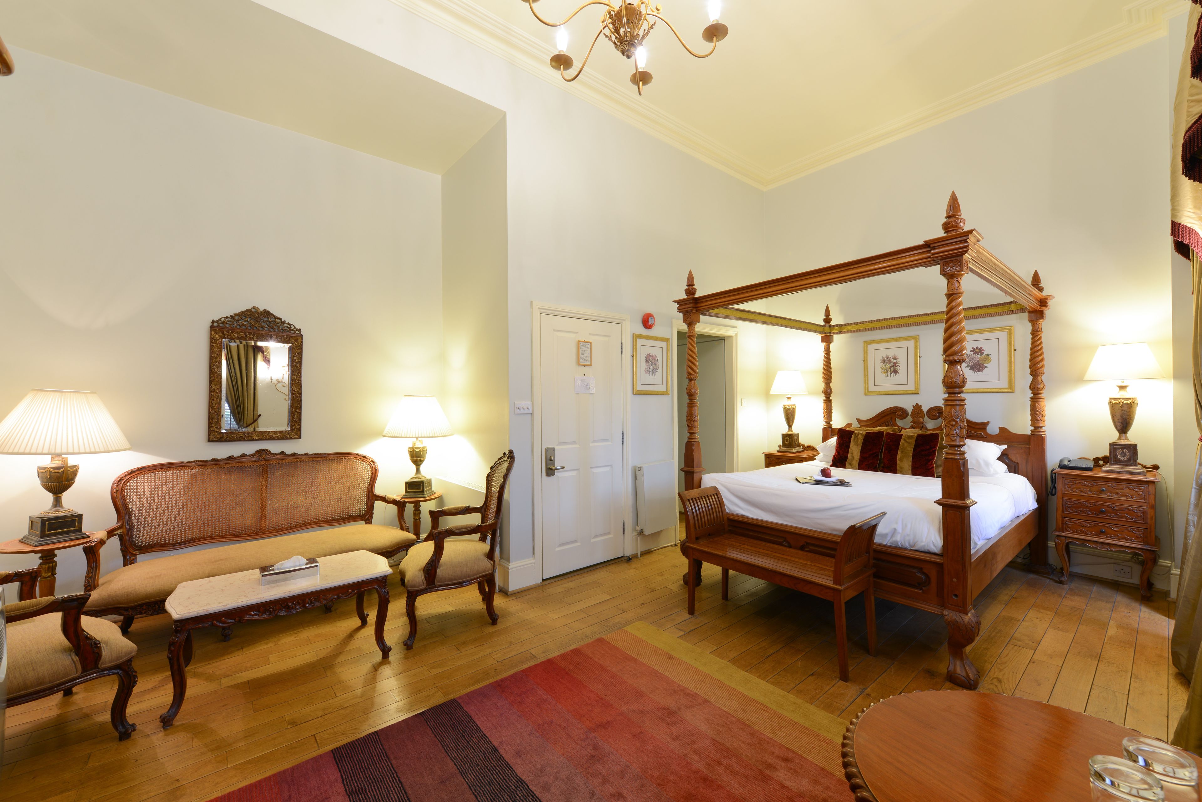 Un dormitorio tradicional con cama con dosel, una zona de estar con sofá y sillones, y una mesa de comedor.