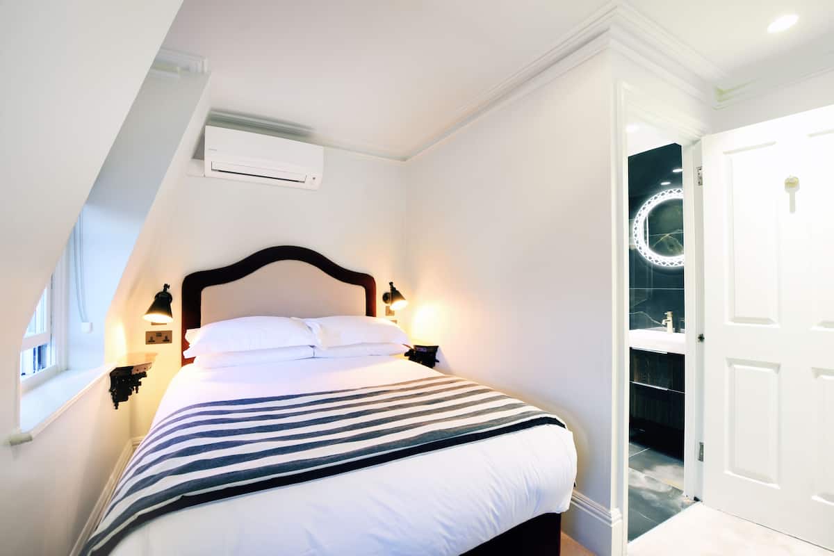 Ein ordentlich bezogenes Bett mit einer gestreiften Decke, einer Nachttischlampe und einer Wand-Klimaanlage.