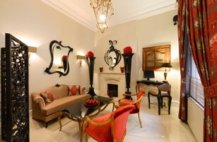 A living room with a sofa, coffee table, and chairs, a fireplace, and decorative mirrors and vases.