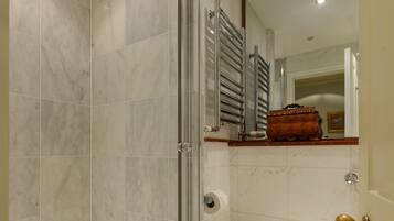 Une salle de bain dotée d’une douche à parois de verre, de toilettes blanches et d’un sol carrelé en marbre.