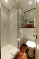 Un bagno con doccia vetrata, un water bianco e un pavimento in marmo.