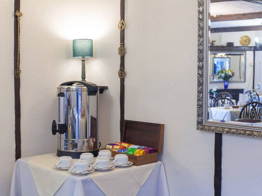 Uma estação de café com uma cafeteira, xícaras e uma caixa de saquinhos de chá sobre uma mesa.