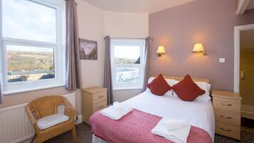 A hotel room with a bed, two bedside lamps, a chair, a window with a view, and a radiator.