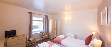 Hotellihuone, jossa on kaksi sänkyä, televisio, työpöytä ja ikkuna, jossa on verhot.