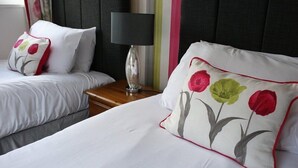 Et hotelværelse med to senge, et natbord med en lampe og et vindue med gardiner.