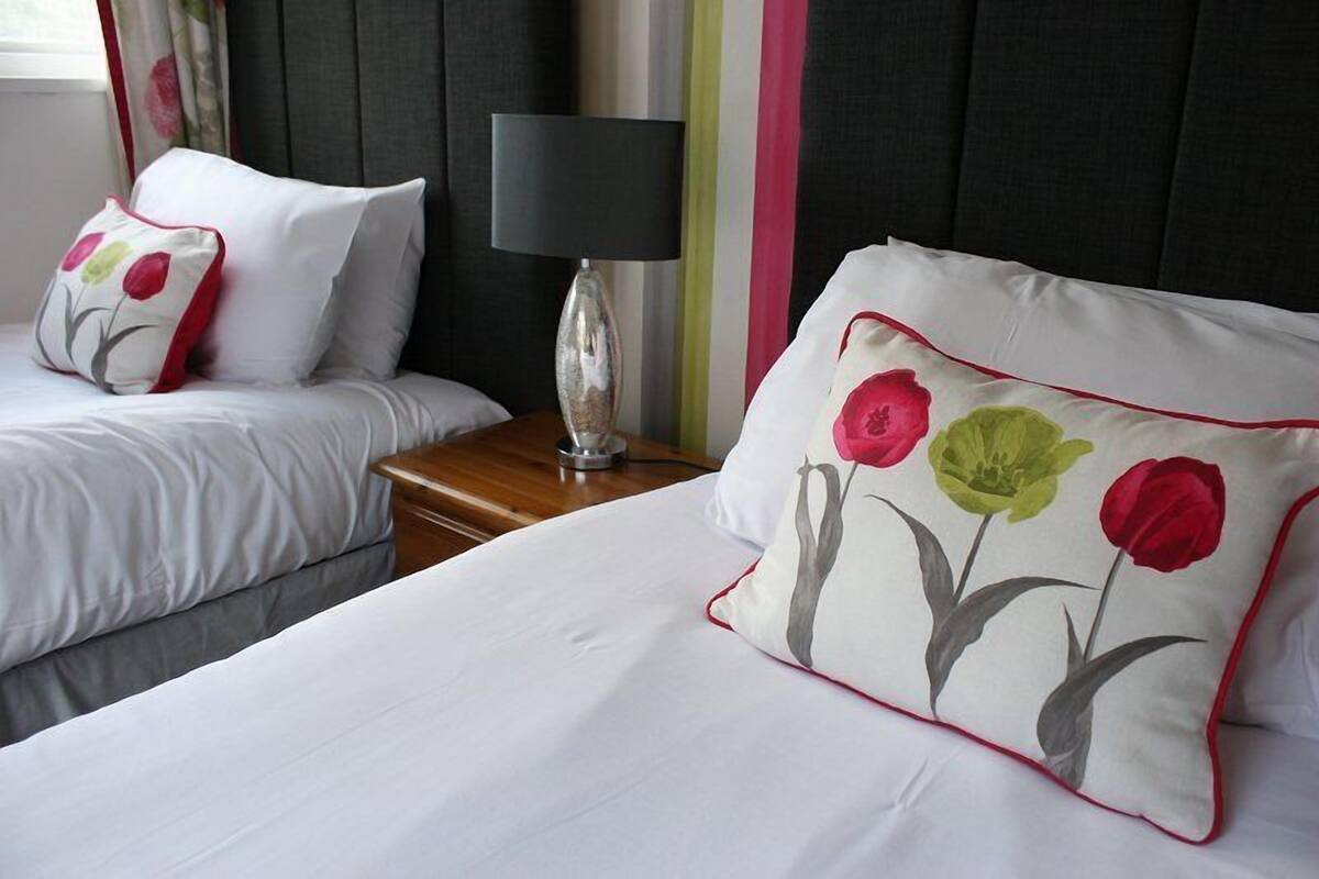 A hotel room with two beds, a bedside table with a lamp, and a window with curtains.