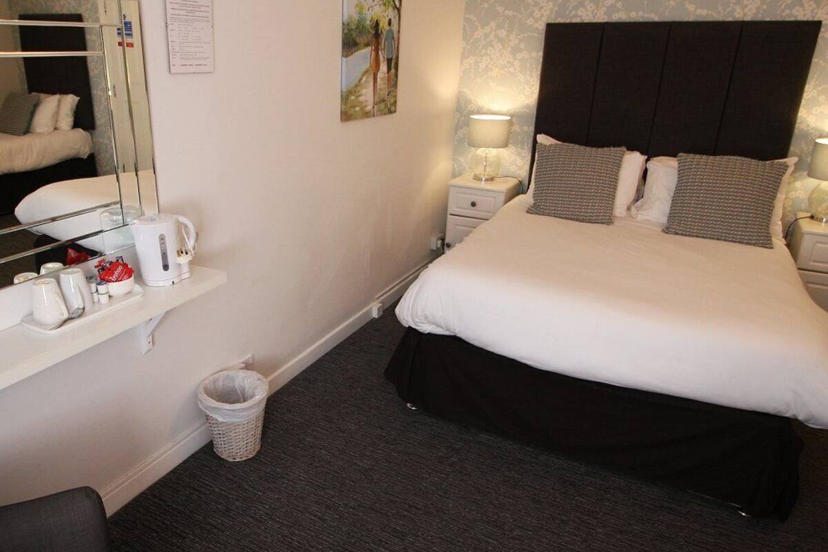 A hotel room with a large bed, bedside tables with lamps, a mirror, a small trash bin, and a shelf with toiletries.