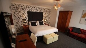 Et soveværelse med en seng, sengeborde med lamper, et trænatbord, et skrivebord, en rød lædersofa og en garderobe.