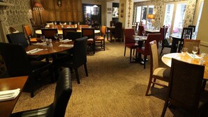 En restaurant med flere spiseborde og stole, tæppede gulve og en hyggelig atmosfære.