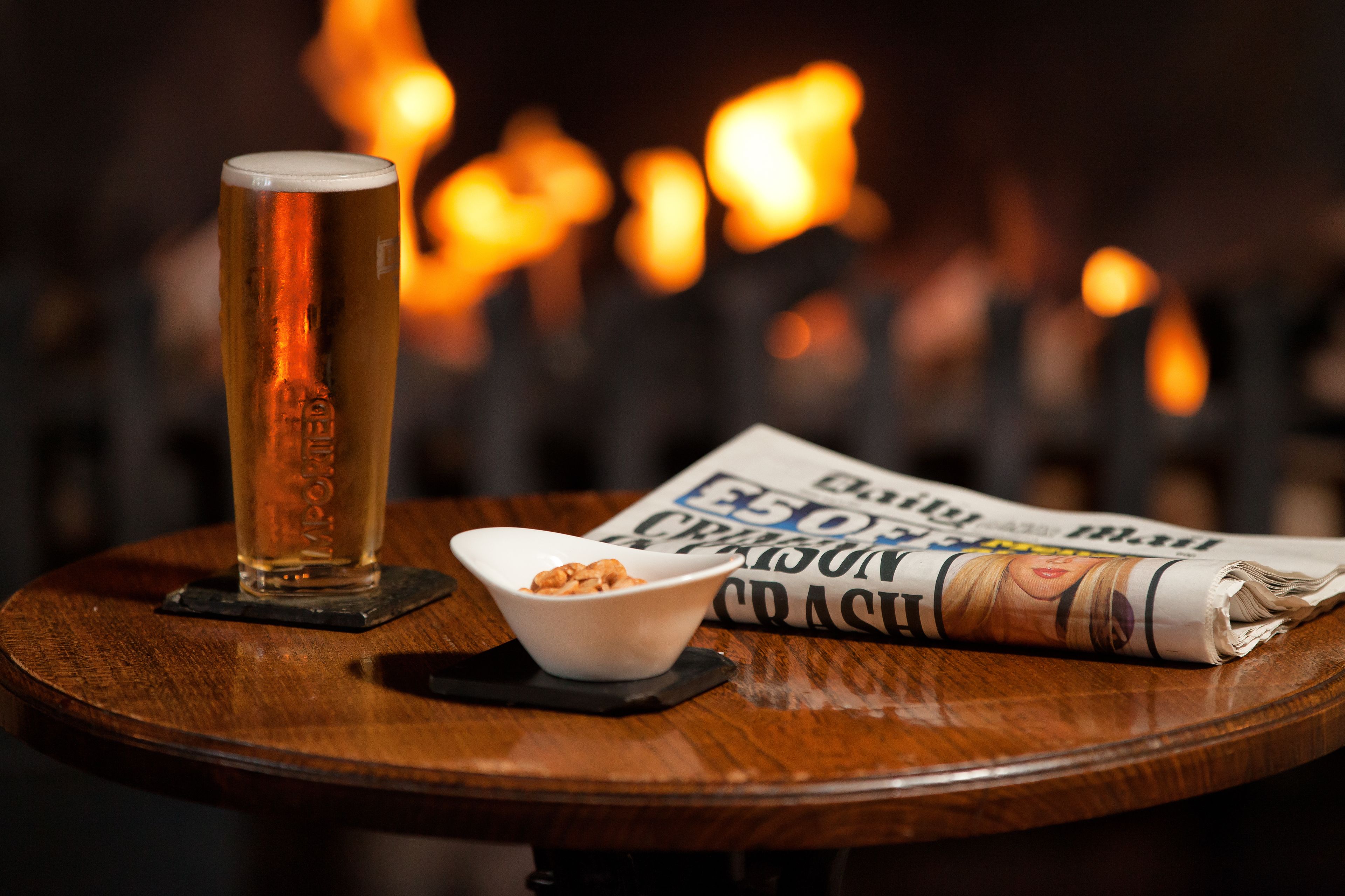 Ein Holztisch mit einem Bierglas, einer Schüssel Nüssen und einer Zeitung.
