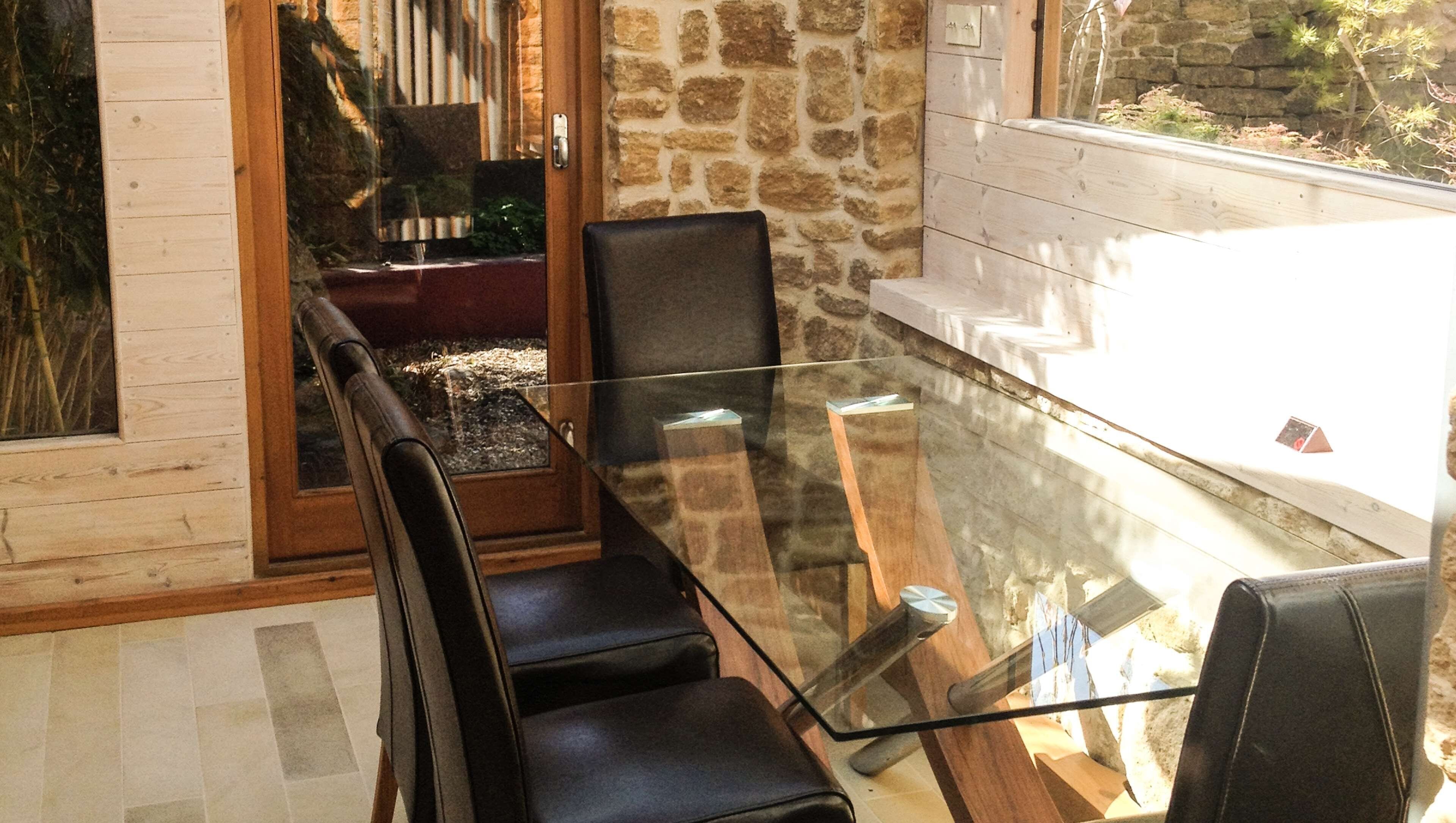 A glass-top table with four black chairs, a stone wall, and a wooden door.