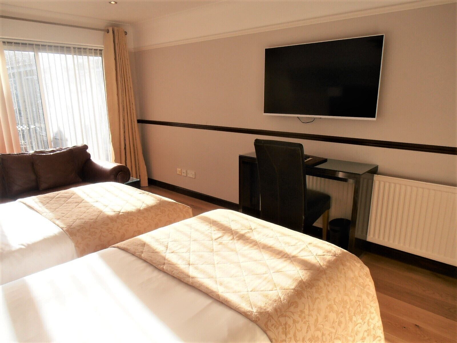 Habitación de hotel con dos camas, un escritorio, una silla, un televisor y una ventana con cortinas.