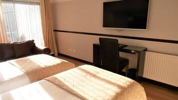 Habitación de hotel con dos camas, un escritorio, una silla, un televisor y una ventana con cortinas.
