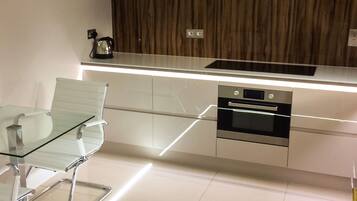 Une cuisine moderne avec une table à manger en verre, des appareils électroménagers en acier inoxydable et un panneau mural en bois.