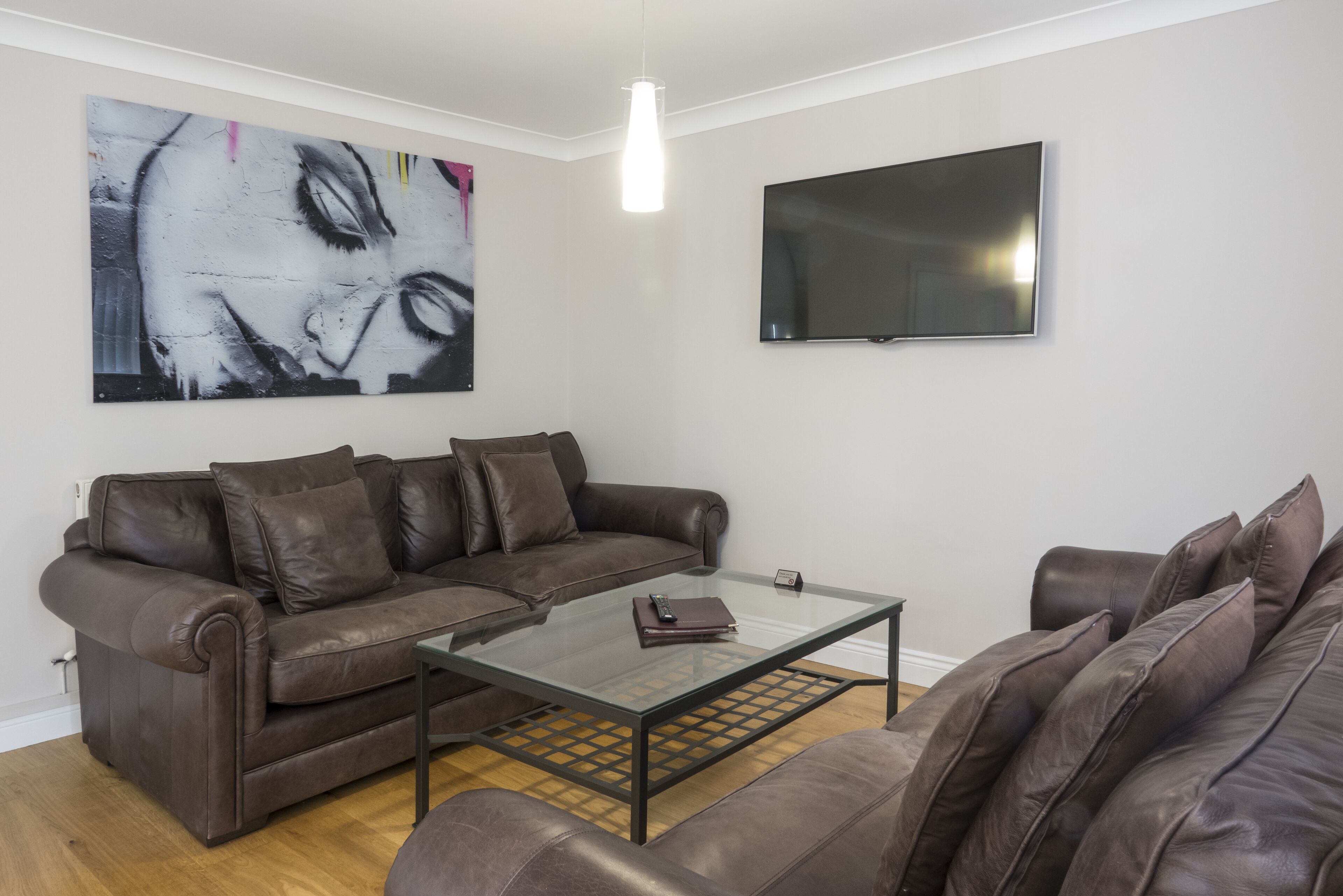 A living room with a brown leather sofa, a glass coffee table, a flat-screen TV, and a large abstract painting on the wall.