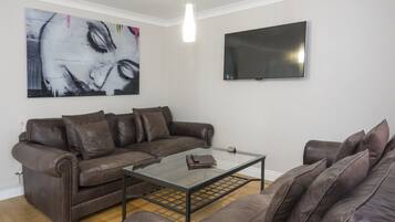 A living room with a brown leather sofa, a glass coffee table, a flat-screen TV, and a large abstract painting on the wall.