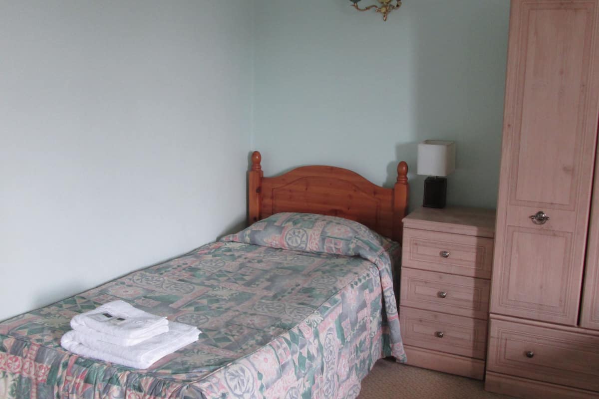 A bedroom with a single bed, a nightstand, a dresser, and a wall-mounted lamp.