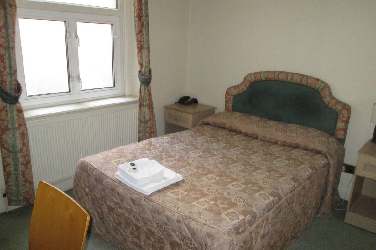 A neatly made bed with a patterned bedspread, a bedside table with a lamp, and a chair.
