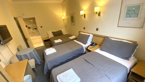Une chambre d’hôtel avec deux lits, une petite table, une chaise, un bureau et un téléviseur.