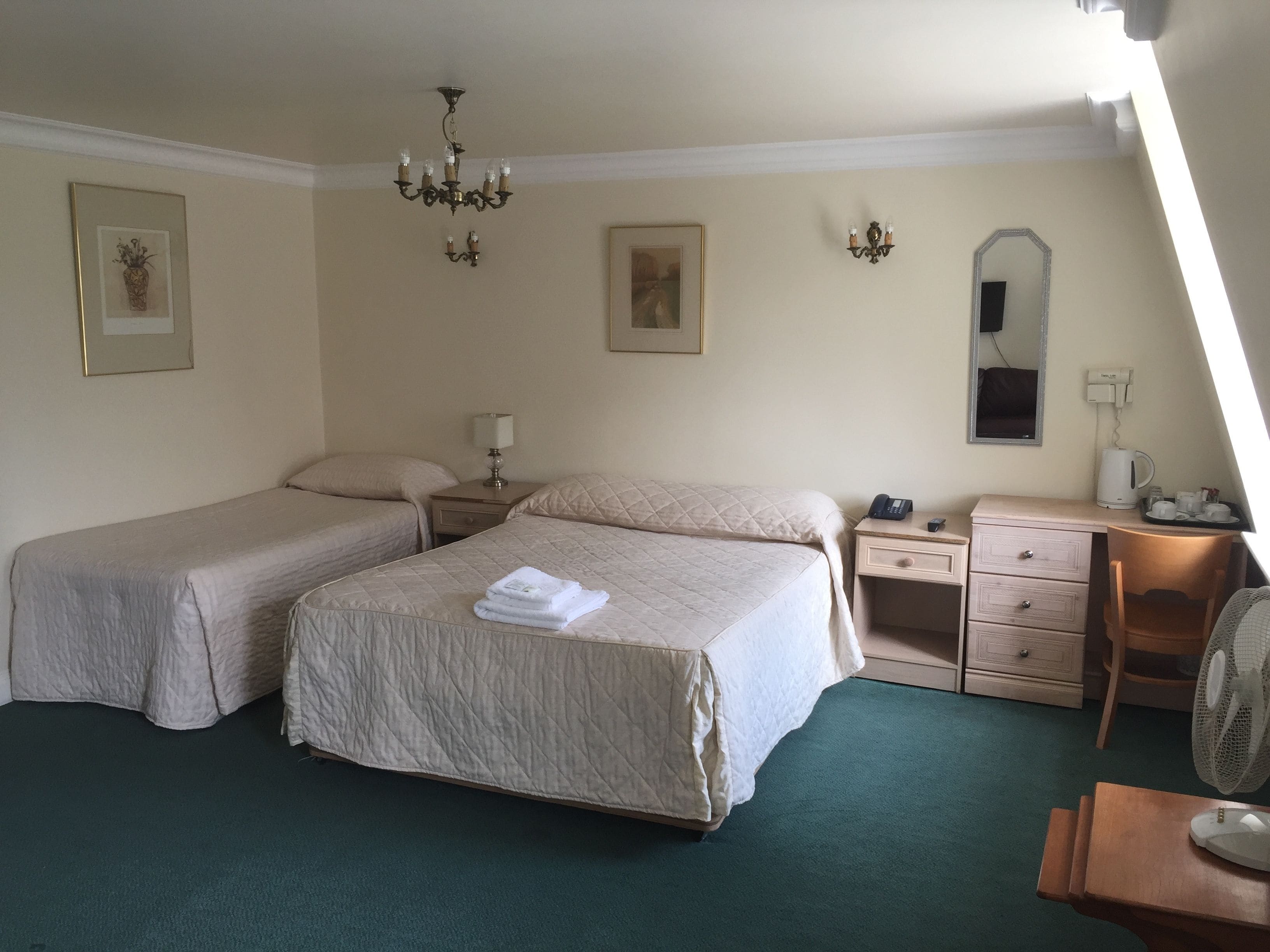 Habitación de hotel con dos camas, un escritorio, una silla, un espejo, un ventilador y una araña.