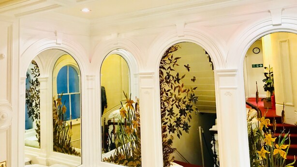 Un vaste hall d’entrée orné de colonnes blanches décoratives, un escalier aux marches rouges et des décorations florales.