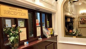 Un comptoir d’accueil à l’hôtel Brompton, avec un panneau indiquant la zone de réception, un panneau interdisant de fumer et des brochures d’information.
