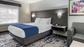 A hotel room with a large bed, bedside lamps, a desk with a phone, a gray armchair, and a window with a view.