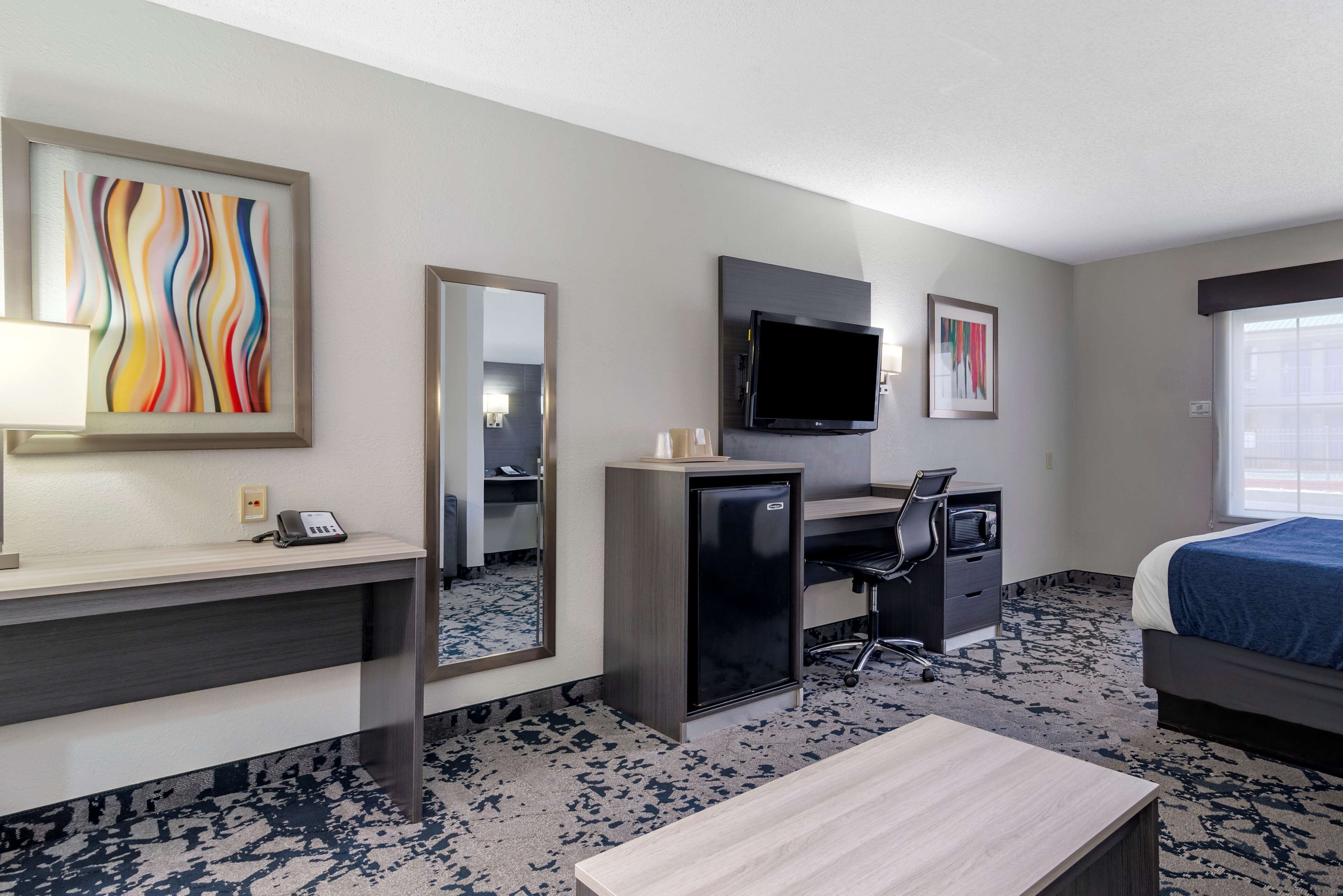 A hotel room with a desk, chair, bed, TV, and artwork on the walls.