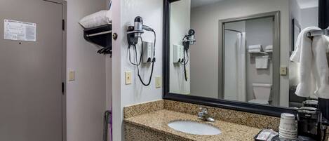 Un baño con encimera de granito, un lavabo, un espejo y un secador de pelo montado en la pared.