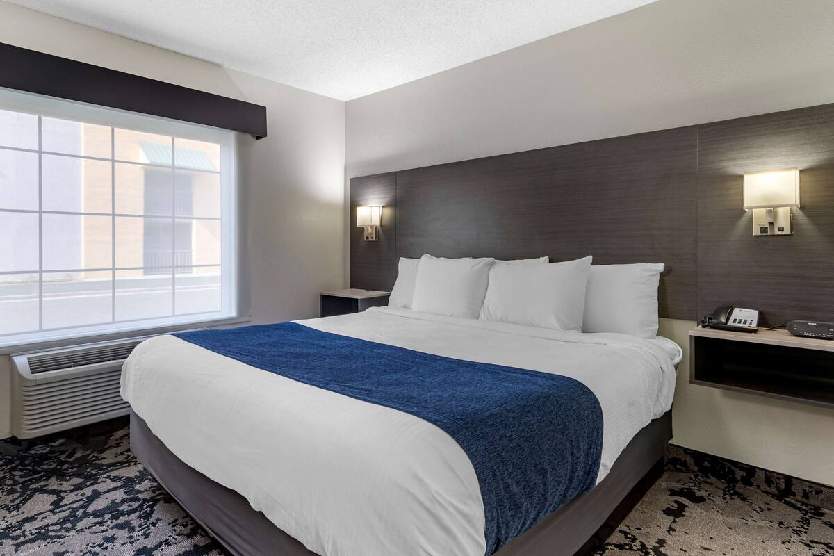 A hotel room with a large bed, a window, a wall-mounted lamp, and a bedside table with a phone.