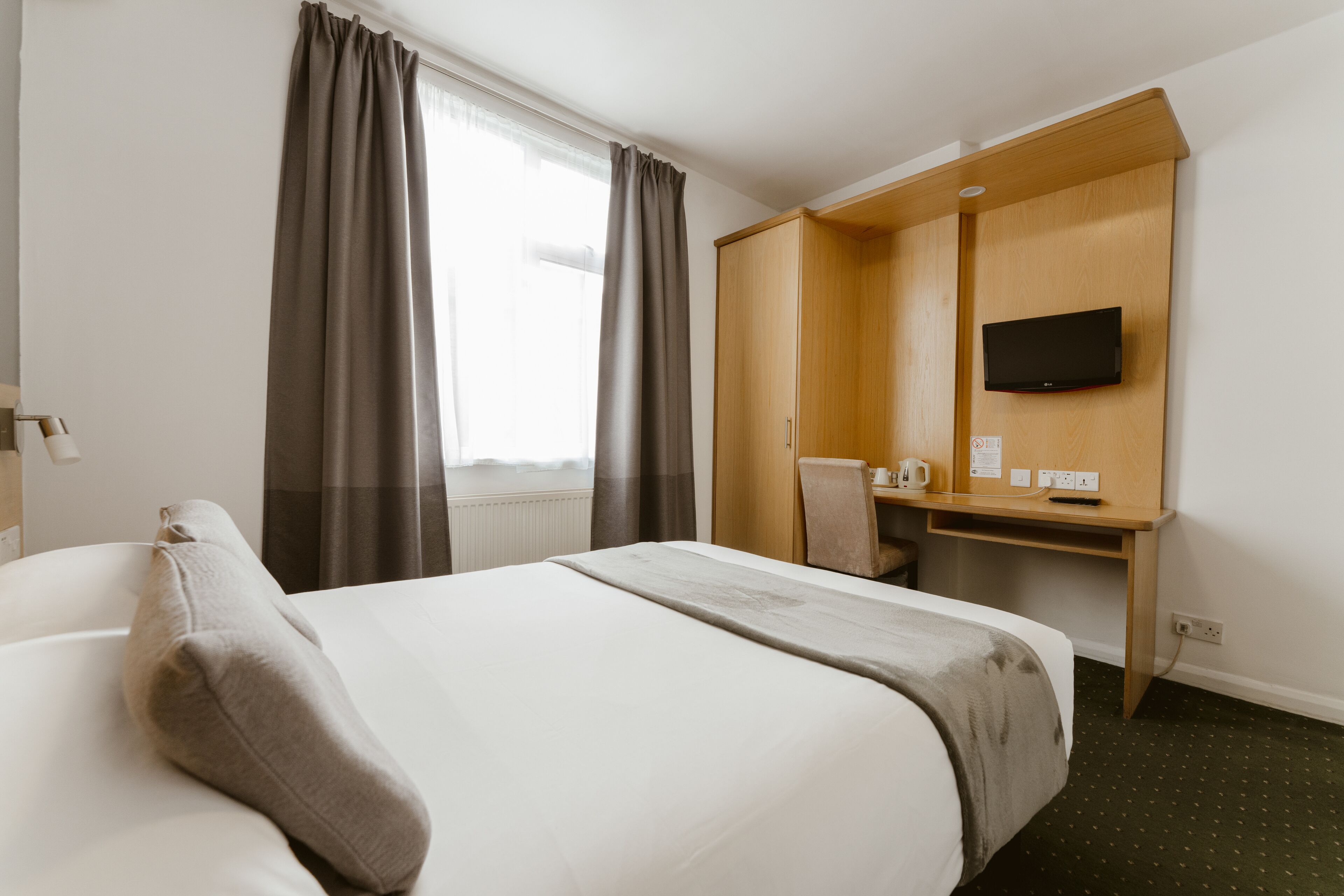 Habitación de hotel con cama, escritorio, silla, televisión y ventana con cortinas.