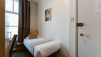 Une chambre d’hôtel avec un lit, un bureau, une chaise, une fenêtre avec des rideaux, un tableau au mur et une porte avec une serrure.