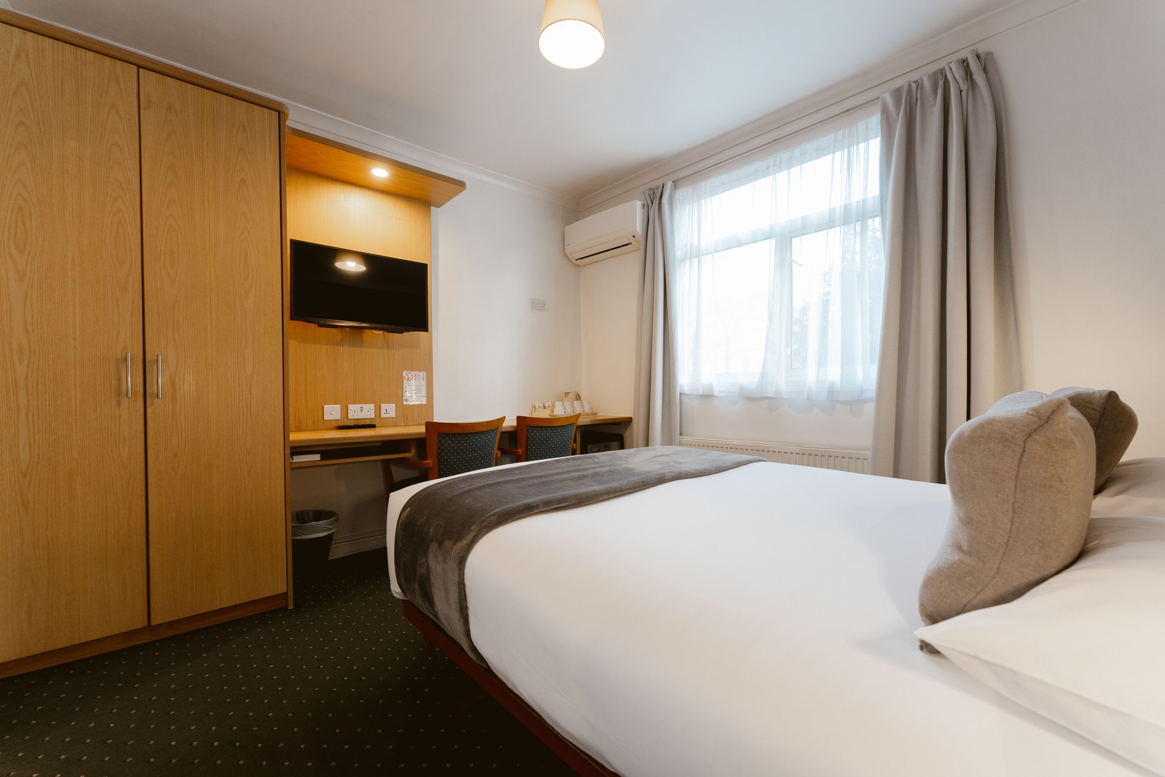 Een hotelkamer met een bed, bureau, stoel, kledingkast en televisie.