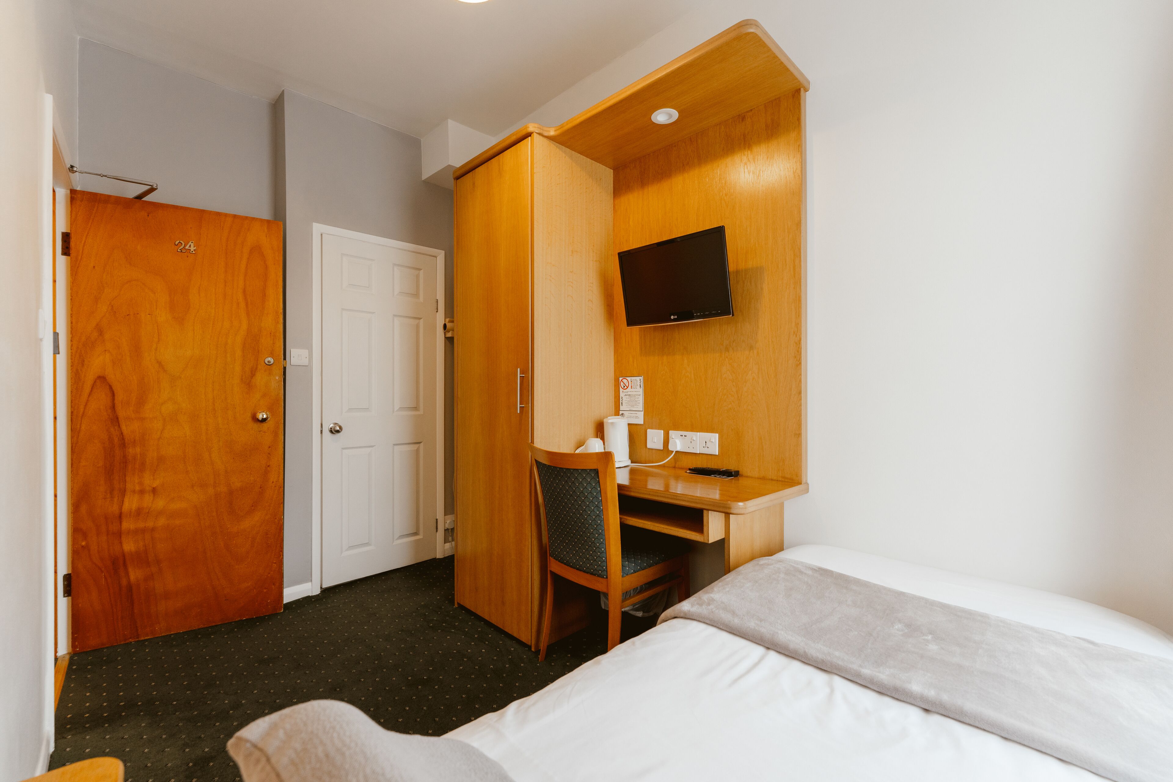 Una habitación de hotel con una cama, un escritorio con una silla, un televisor y una puerta.