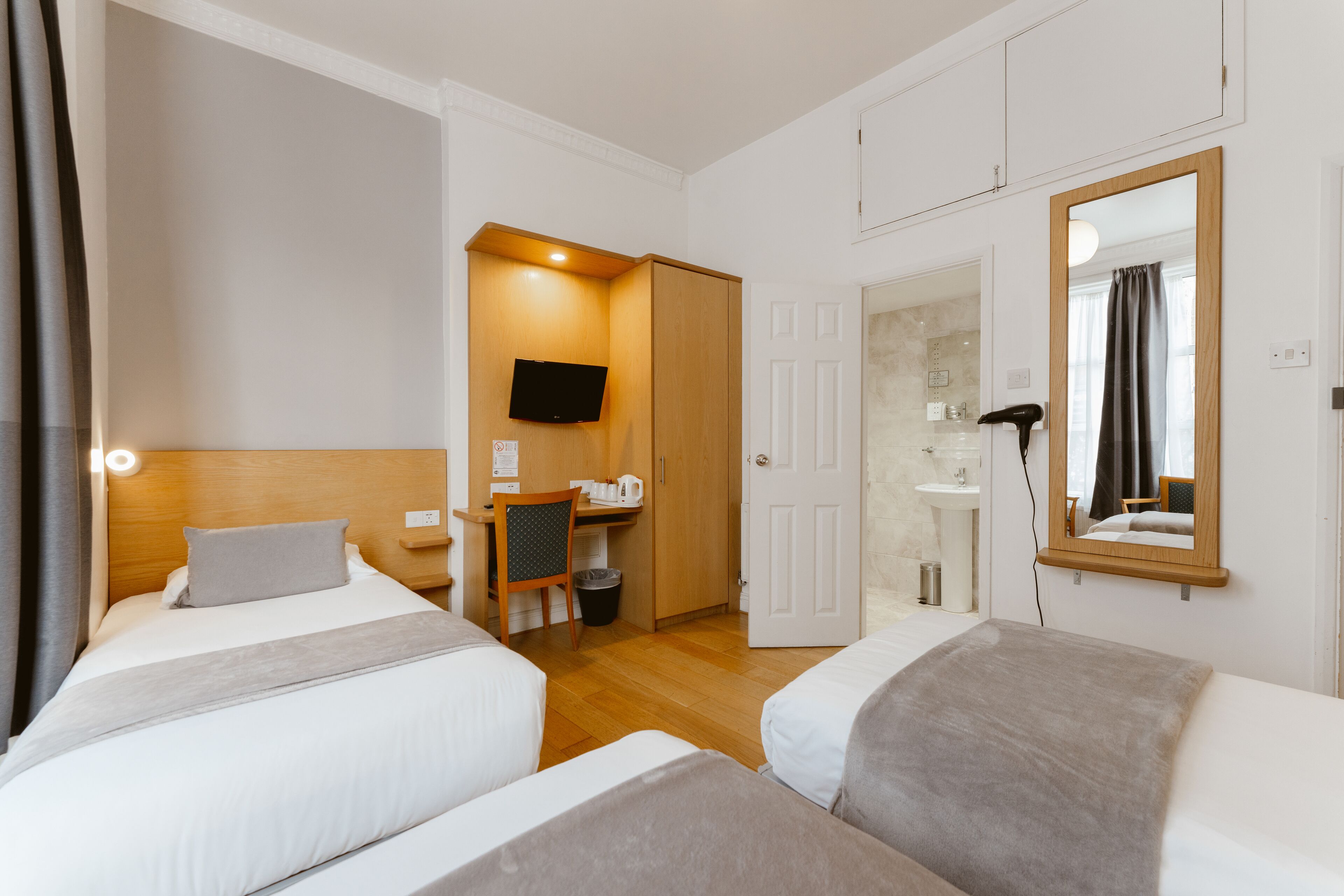 Camera d'albergo con due letti, una scrivania, una televisione, uno specchio e un bagno parzialmente visibile.
