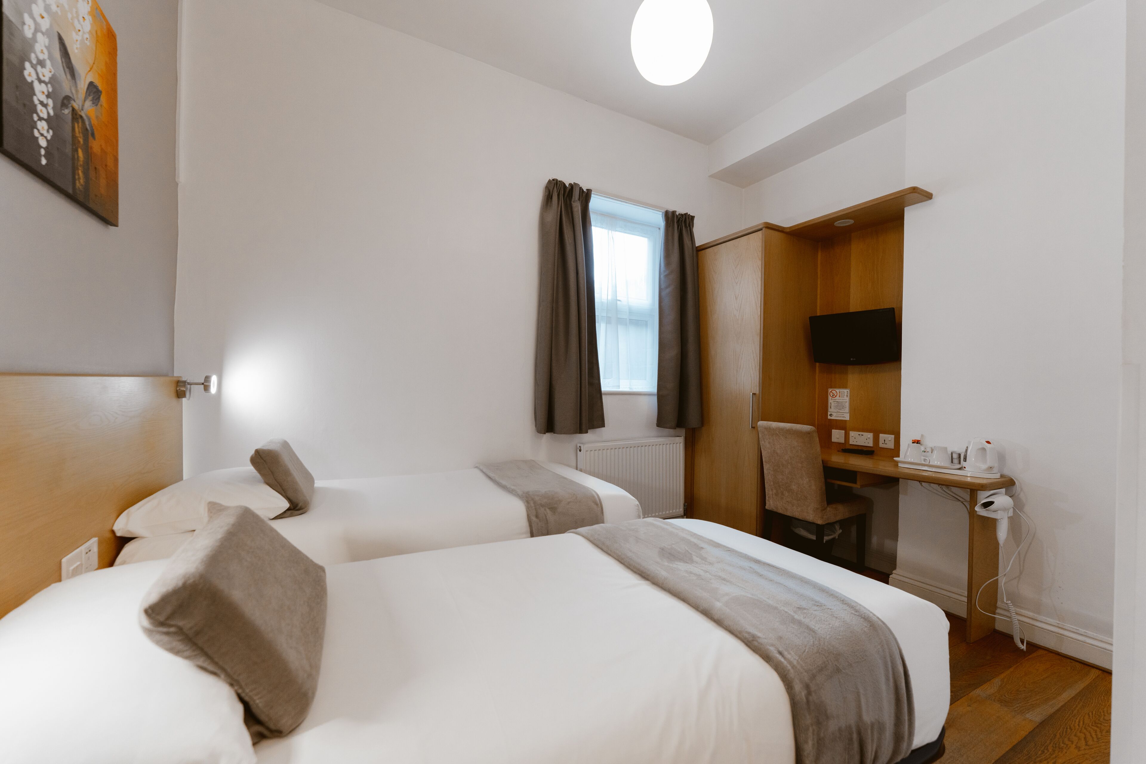 Una camera d'albergo con due letti, una scrivania con una sedia, una televisione e una finestra con tende.