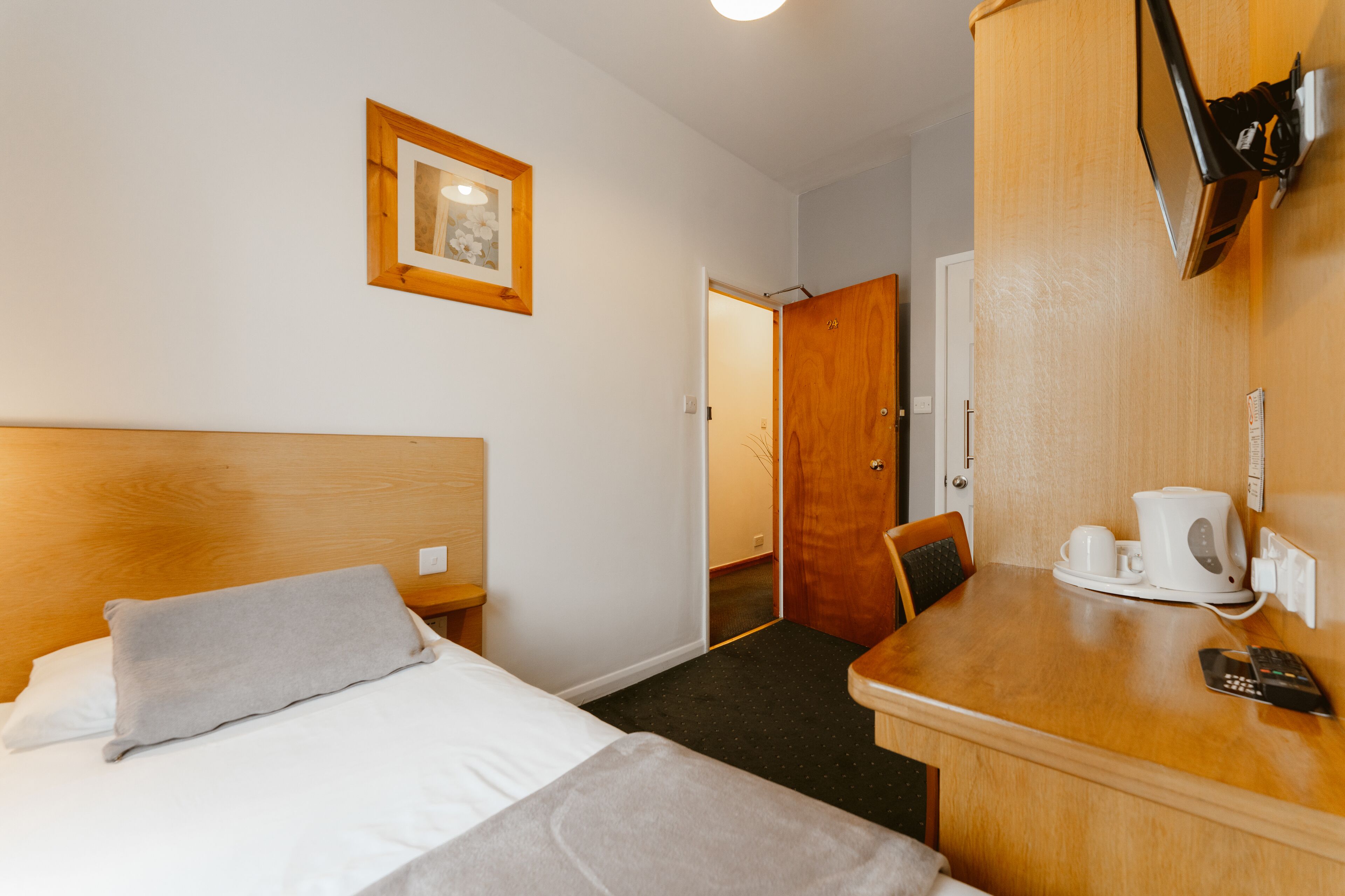 Une chambre d’hôtel avec un lit, une table de chevet équipée d’une machine à café, une télécommande et un tableau encadré au mur.