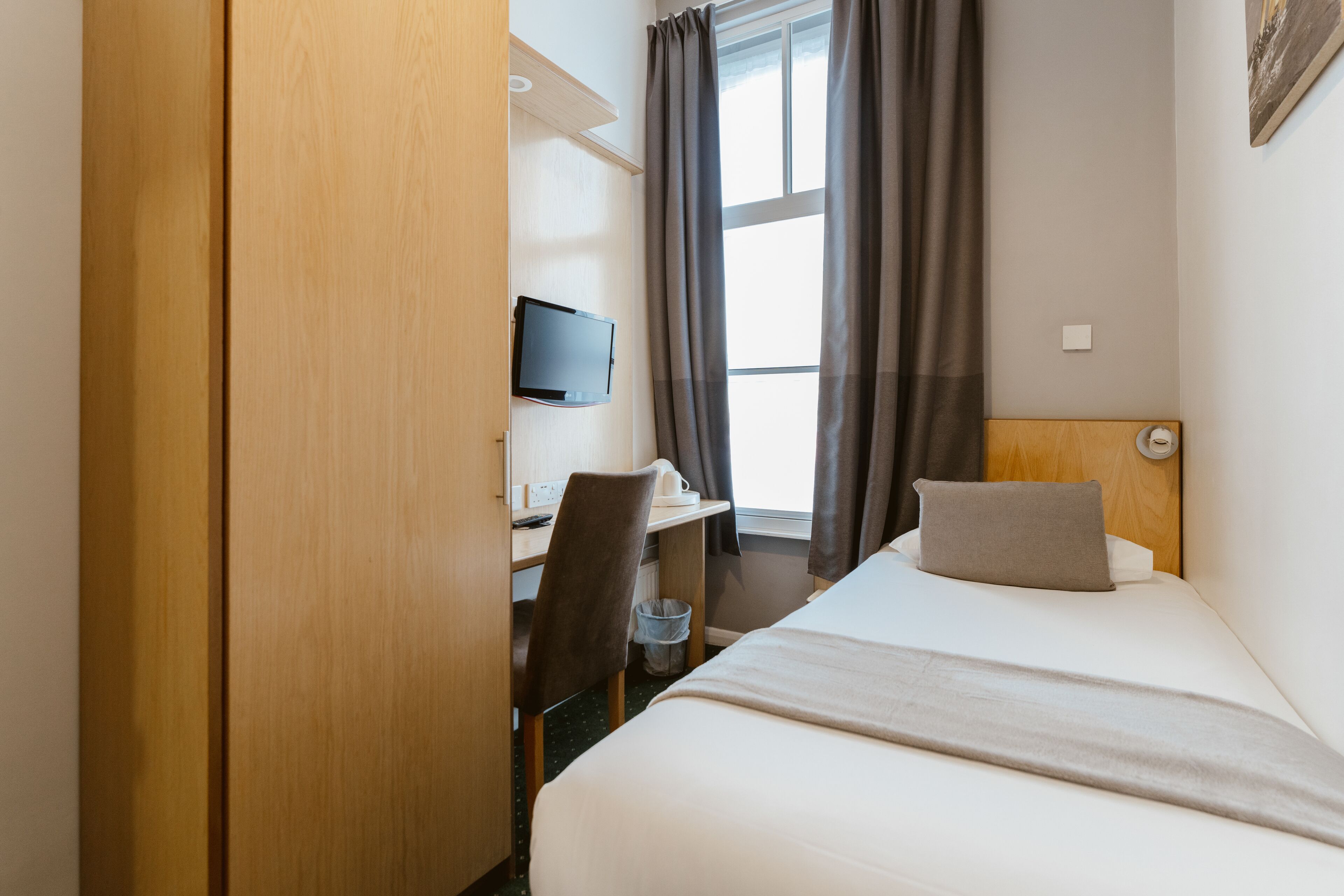 Habitación de hotel con cama, escritorio con silla, televisor y ventana con cortinas.