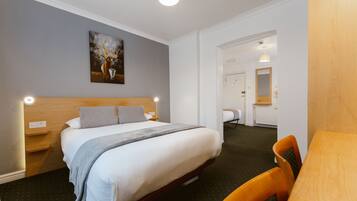 Een hotelkamer met een bed, nachtkastjes, een schilderij, een spiegel en een houten tafel.