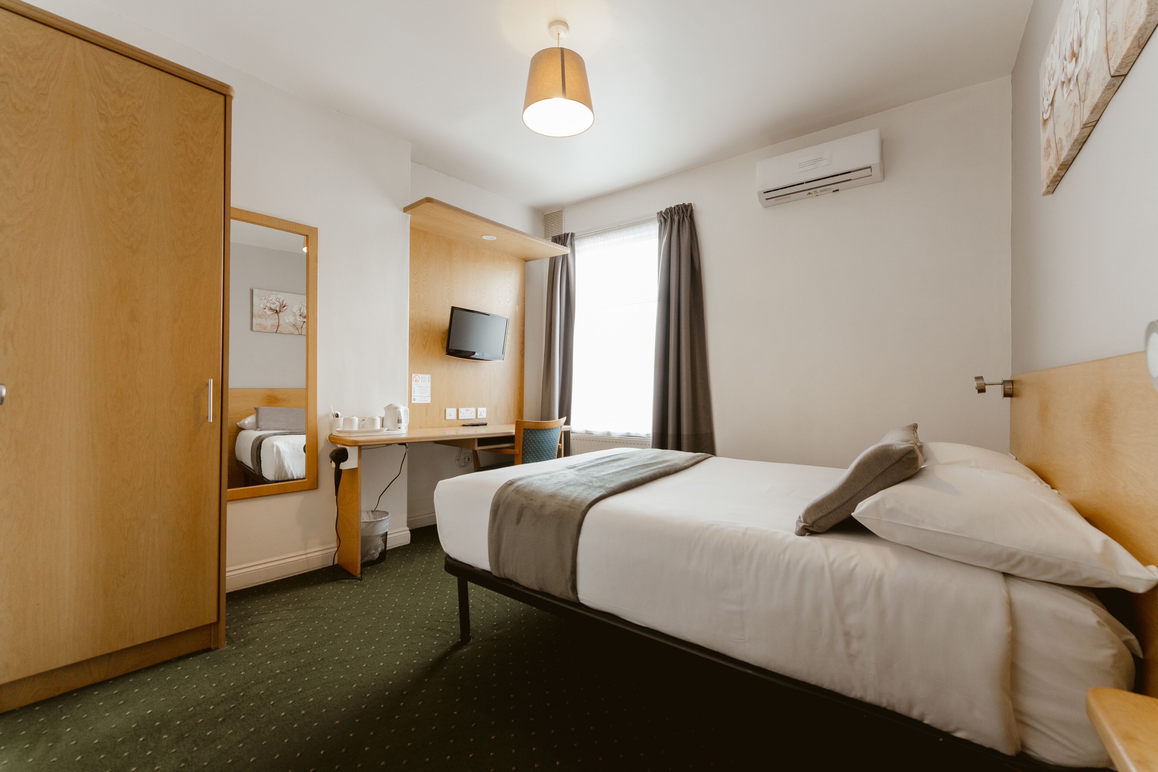 Hotelkamer met een bed, bureau, stoel, kast, televisie en een raam met gordijnen.