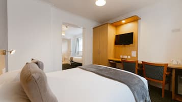 A hotel room with a bed, a desk, a chair, a television, and a wardrobe.