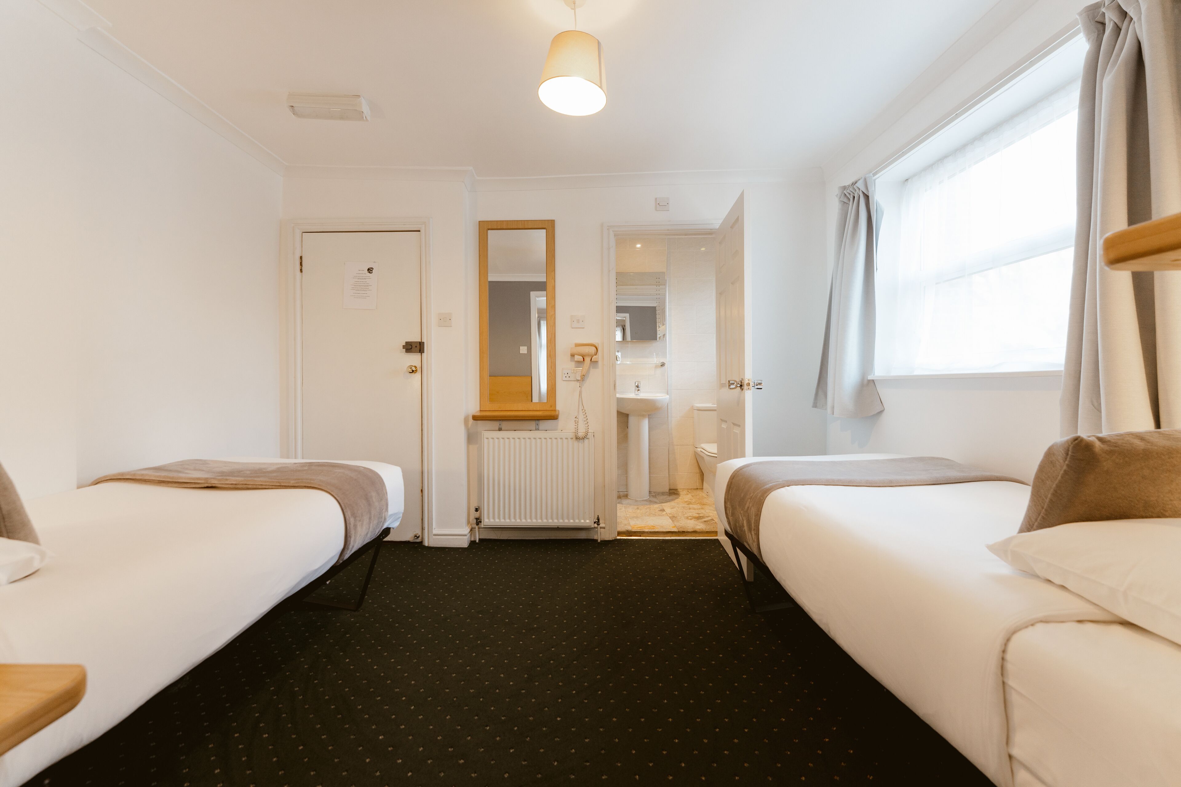 Une chambre d’hôtel avec deux lits simples, une salle de bain, un miroir et une fenêtre avec des rideaux.