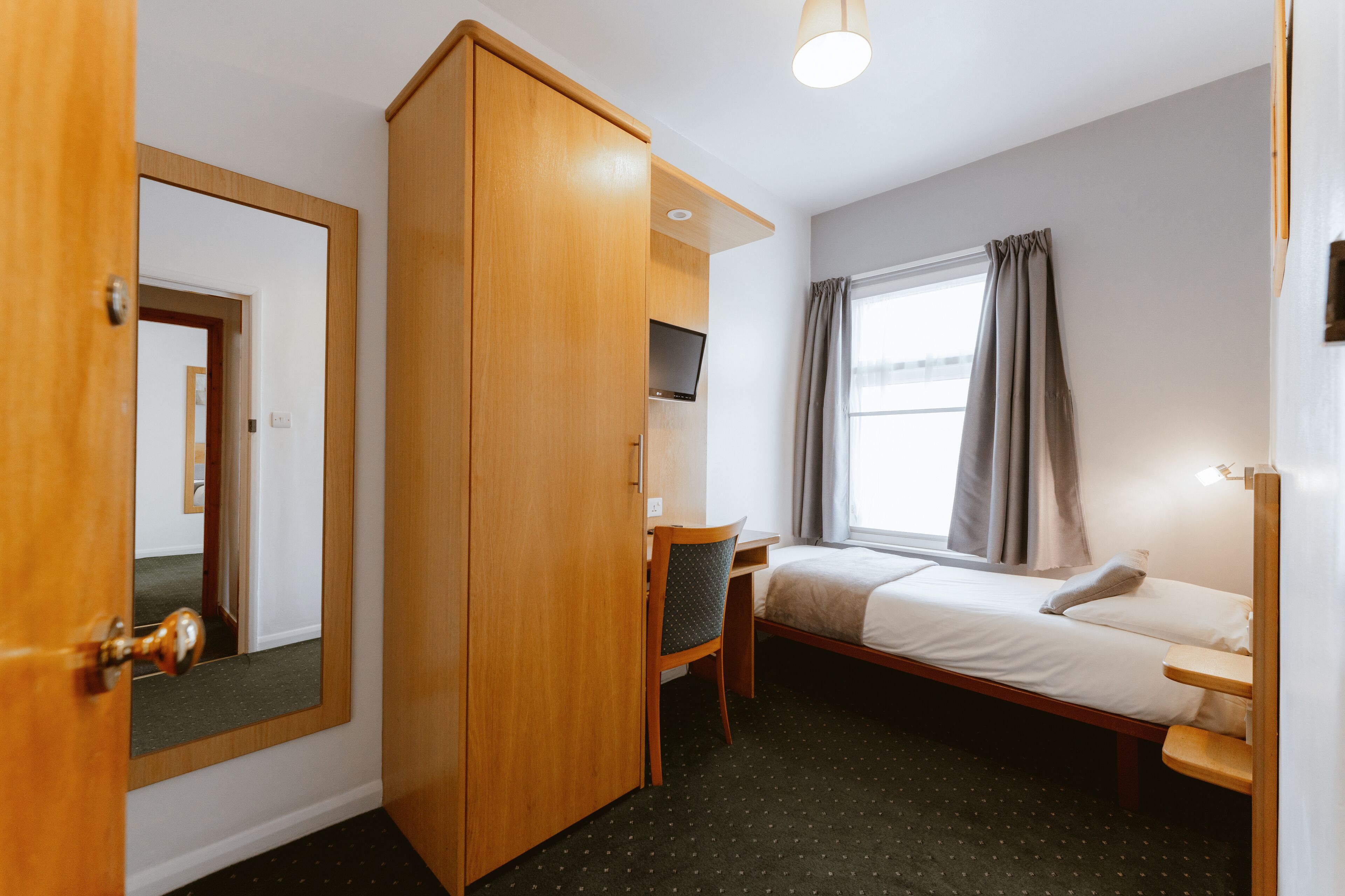 A hotel room with a bed, a desk, a chair, a wardrobe, a television, and a window with curtains.