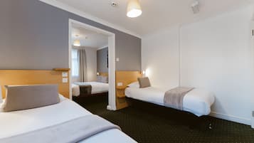 Ein Hotelzimmer mit zwei Einzelbetten, einem Holzkopfstück, einem Spiegel und einer Tür zu einem weiteren Raum.