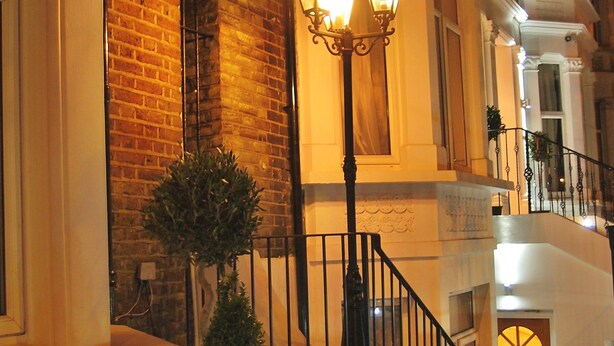 A building with a brick facade, a staircase with a black railing, and a street lamp with three lights. - Hotel 65 (London)