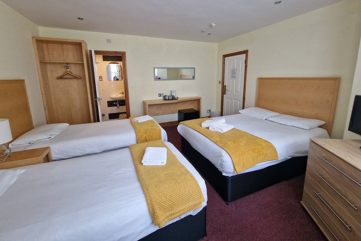 A hotel room with two beds, a wooden dresser, a desk with a mirror, and a hanging coat rack.