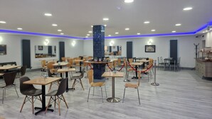 A spacious indoor dining area with multiple tables and chairs, a central decorative pillar, and a modern ceiling design with recessed lighting. - Hotel 65 (London)