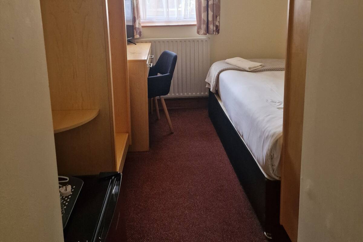 A hotel room with a bed, a desk, a chair, and a radiator.